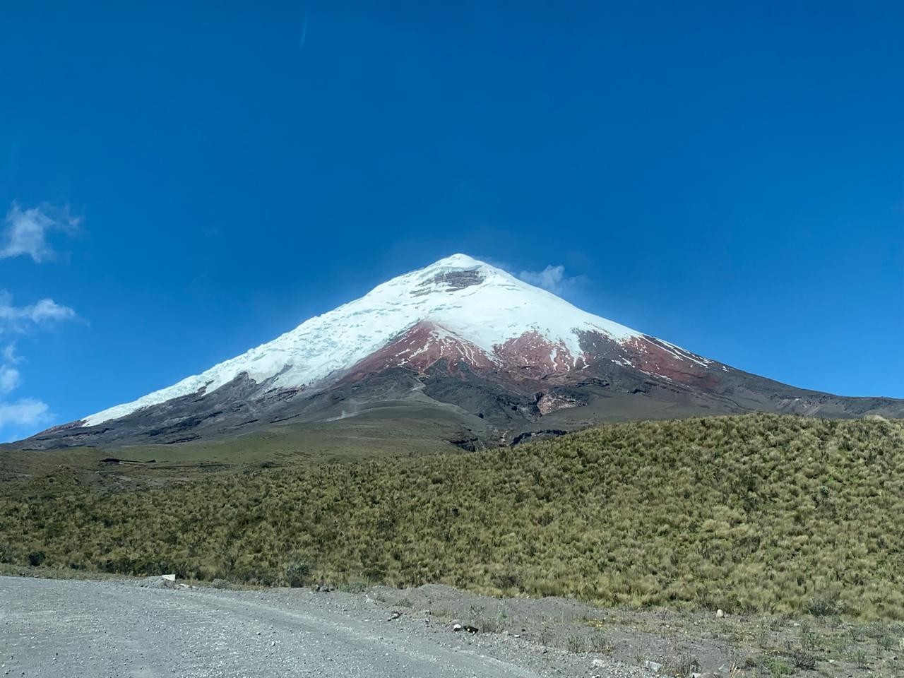 Snow-covered mountain under a clear blue sky, with a scrubby plain and a gravel road in the foreground.